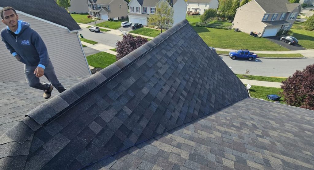 Worker climbs a sloped roof in a residential neighborhood, performing roofing work.