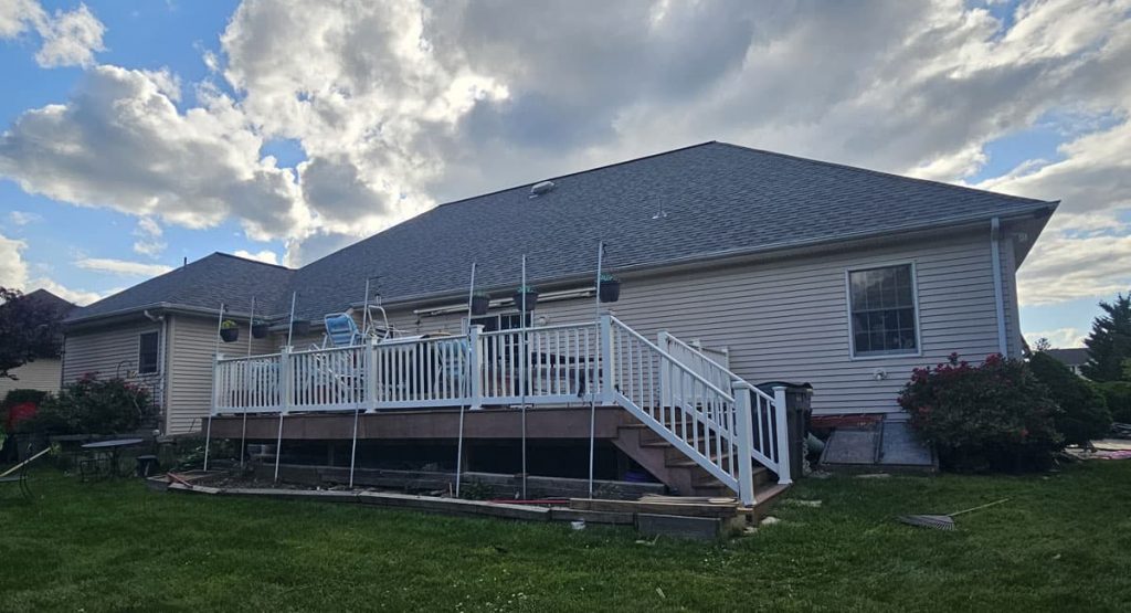 Backyard of a house with a long white-railed deck under construction and scaffolding along the edge.