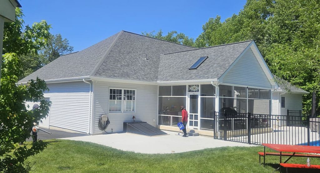 White house with a screened porch and gray roof; a person in a red shirt carries a blue bag near the entrance.