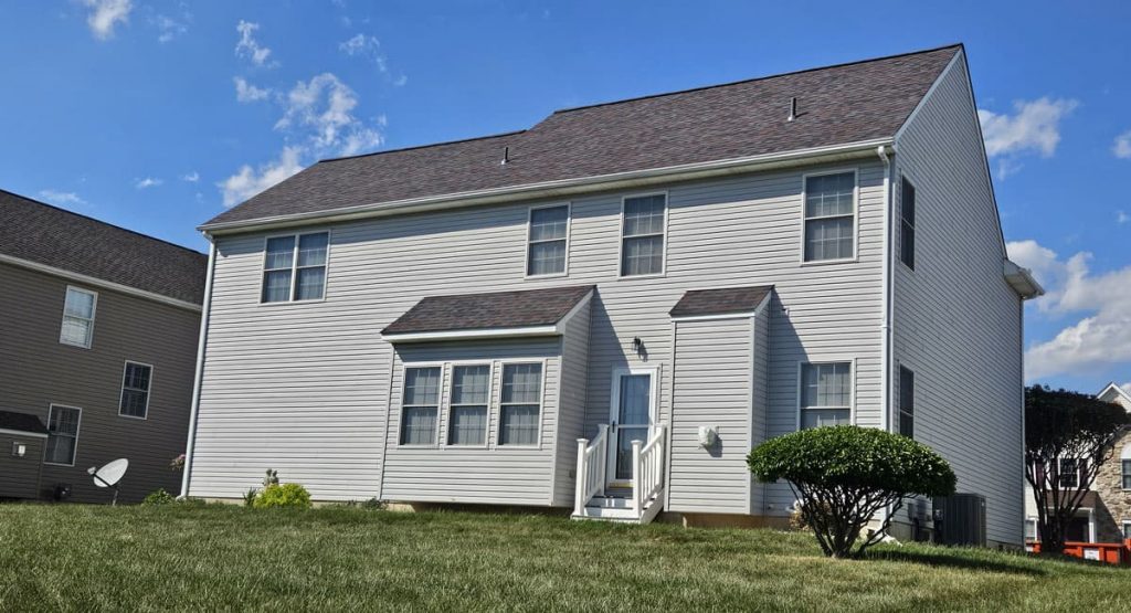 Two-story gray siding house with a small front porch and a manicured shrub, under a blue sky with clouds.