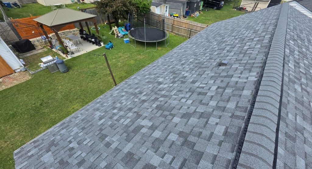 Aerial view of a grey shingle roof with a backyard featuring a trampoline, gazebo, and lawn beyond the houseoutlines.