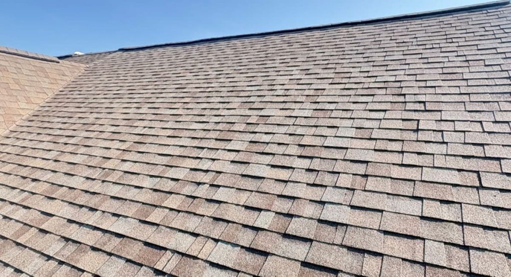 Sloped roof covered with brown asphalt shingles under a clear blue sky